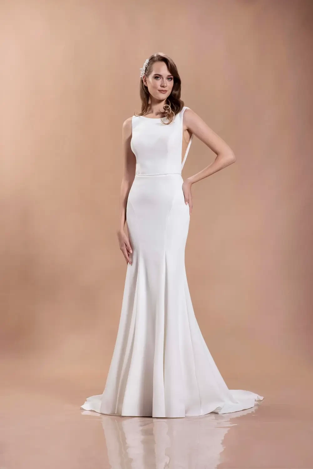 A model wearing a fitted white wedding dress with long sleeves and an off-the-shoulder neckline, standing against a neutral background.