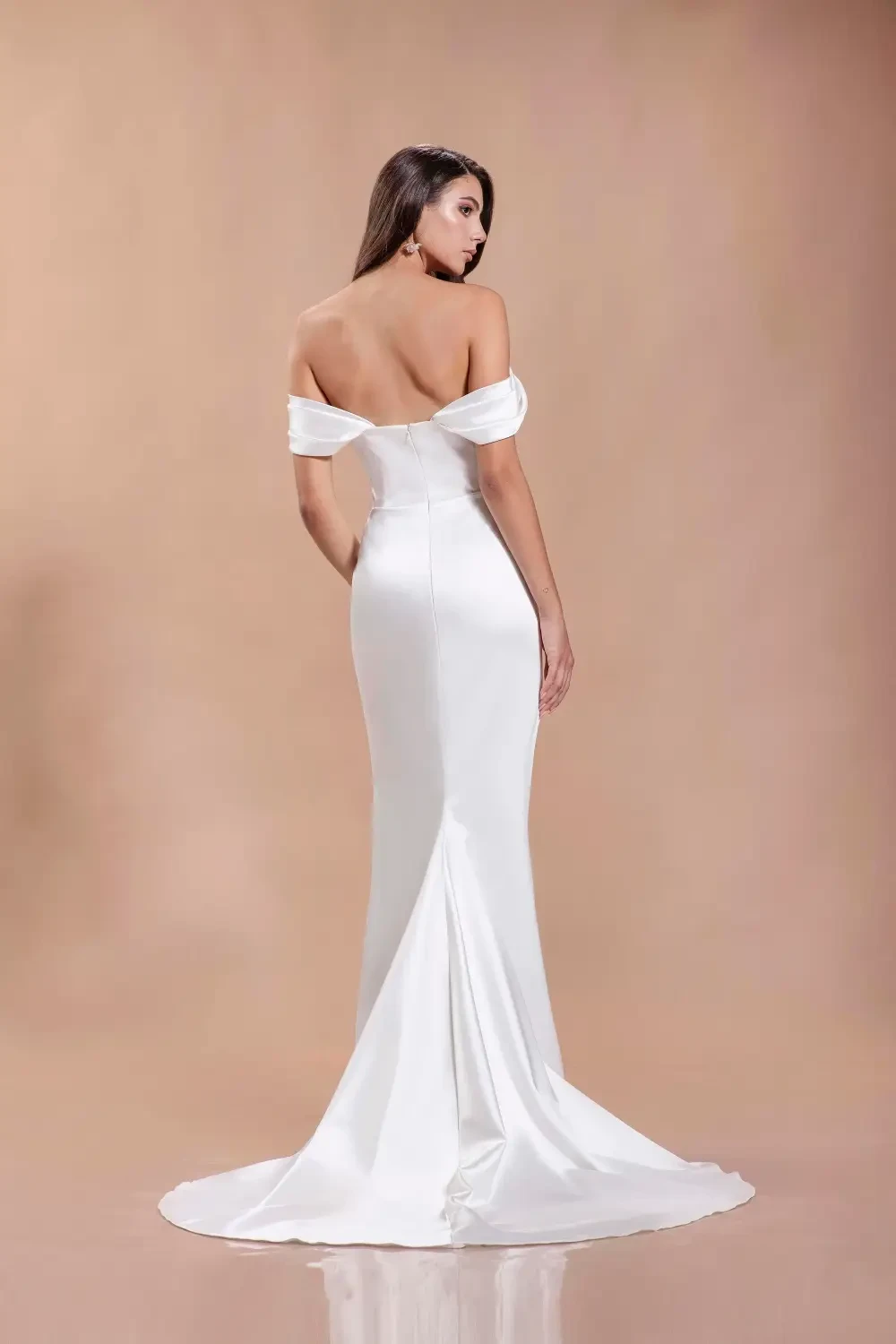 A woman modeling a white off-shoulder gown, showcasing the back of the dress with a long train, against a light, neutral background.