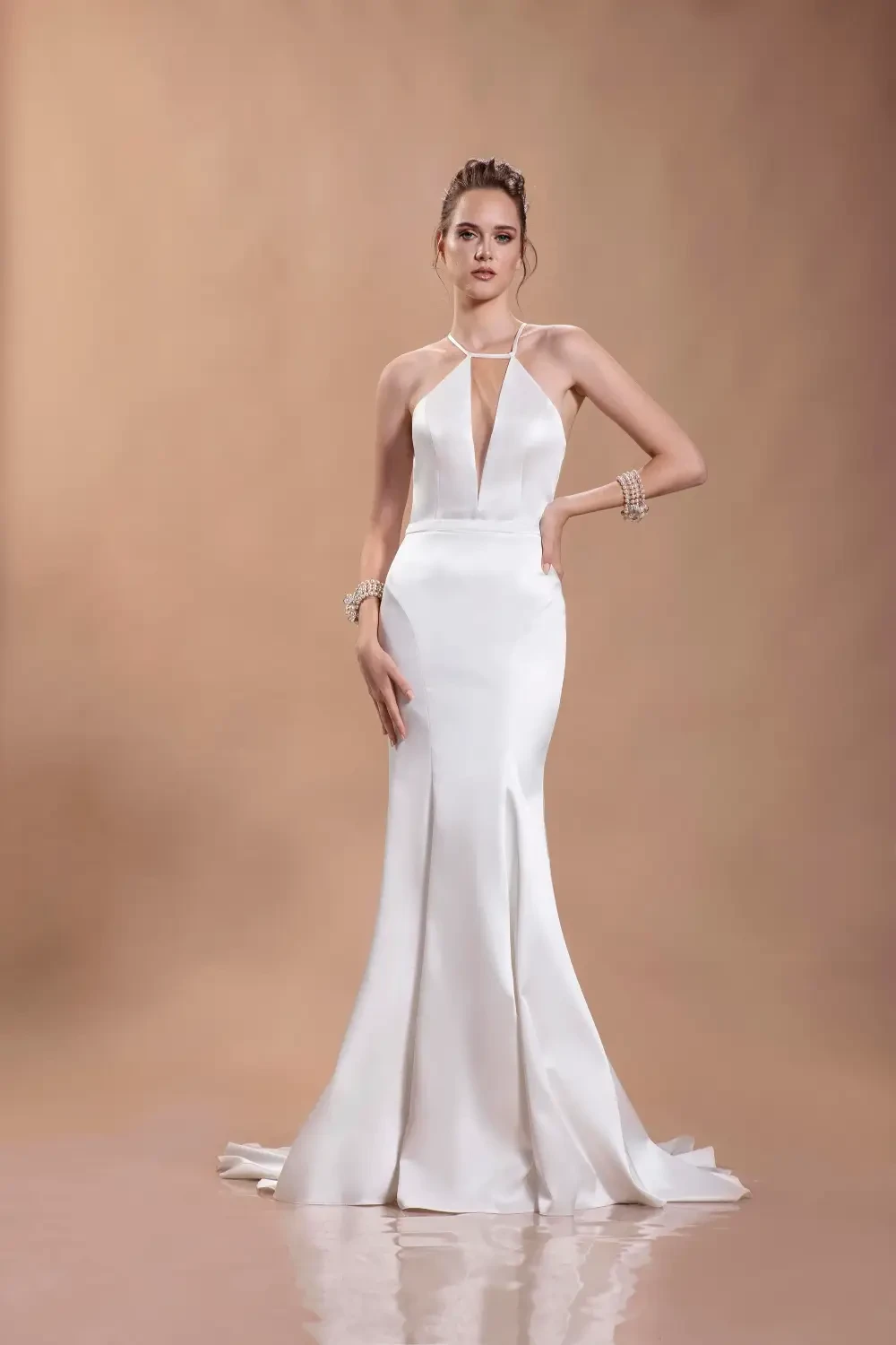 A model wearing a sleek white gown with a halter neck and a fitted silhouette, posed against a neutral background.