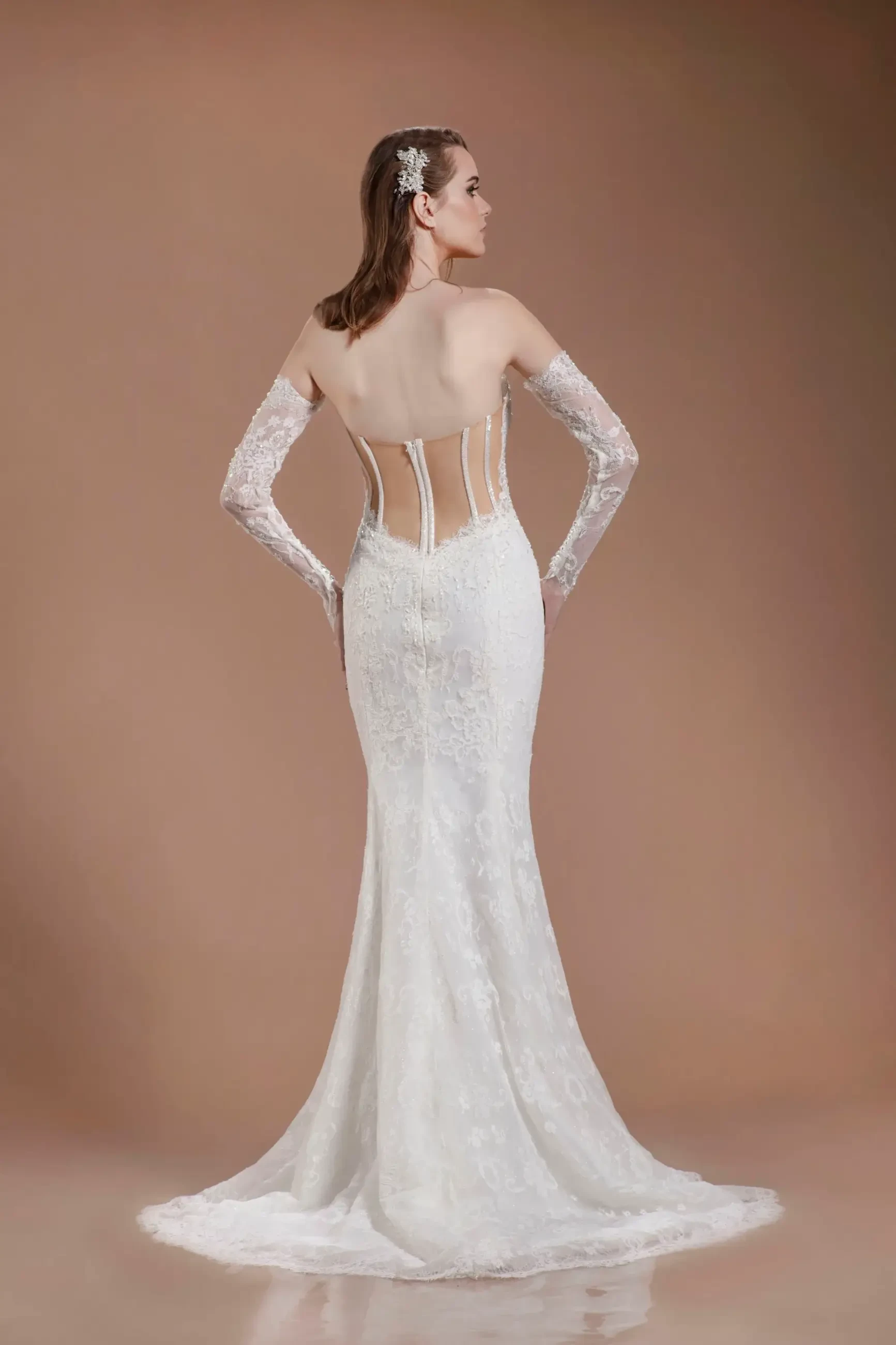 Model is wearing a strapless gown with off-the-shoulder lace gauntlet sleeves, a plunging corset bodice, illusion back panels, and a sweeping train.