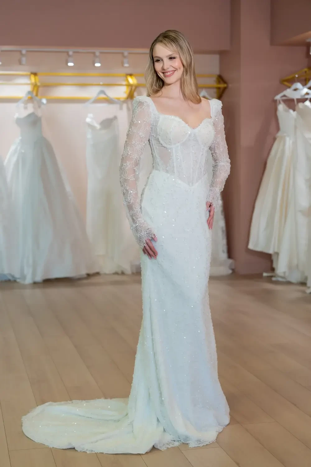 A woman in a white wedding dress with long, beaded sleeves, standing in a bridal shop.
