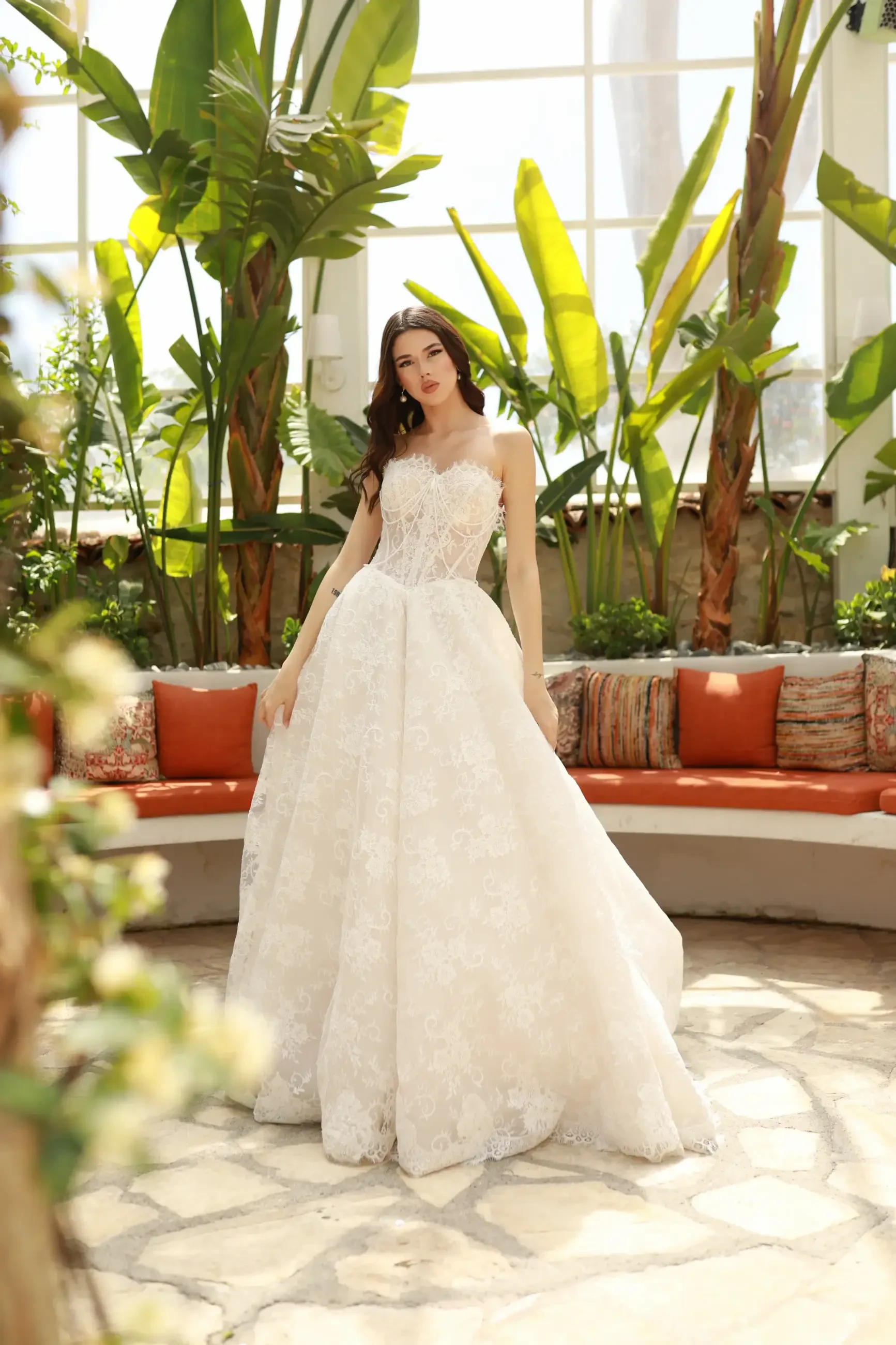 Model is wearing a structured corset bodice gown with lace appliqué and pearl-threaded details, a voluminous tulle skirt, and sheer ruched gloves.